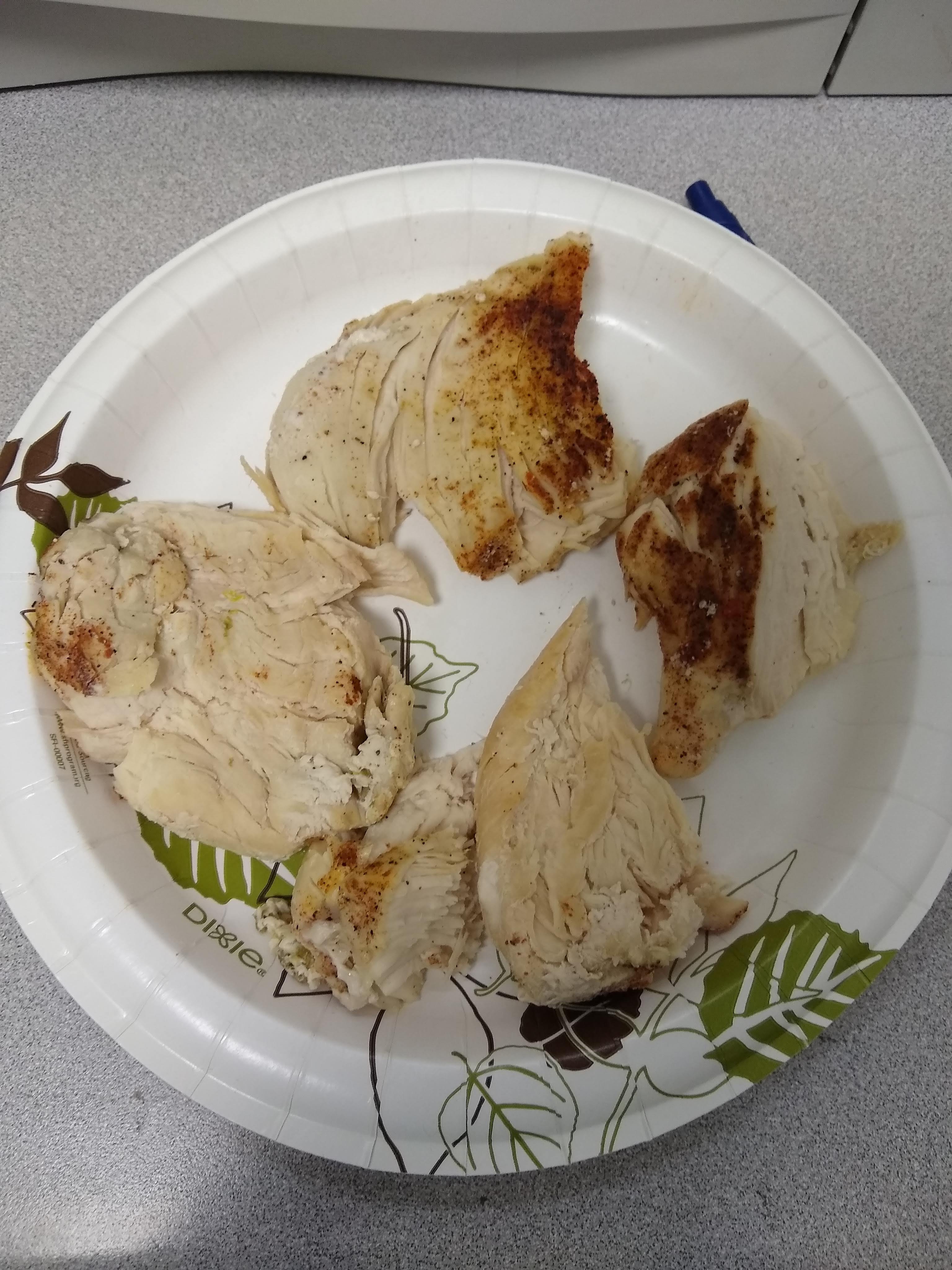 fully cooked and seasoned chicken breast on a paper plate that have been smashed with a human fist.